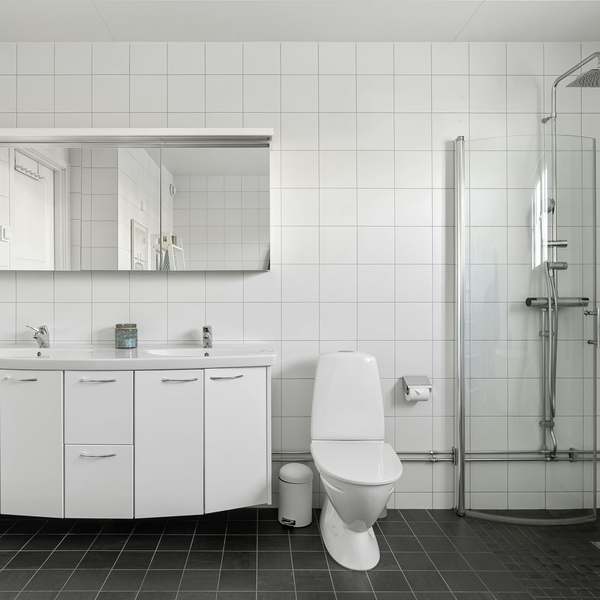 White-tiled bathroom with a double vanity unit, wall-hung toilet and a curved glass shower enclosure