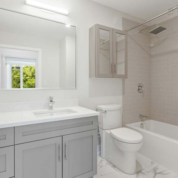 Bright family bathroom with a grey shaker vanity, quartz worktop and a bath with a rainfall shower above