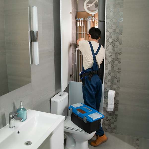 Plumber in overalls working on the pipework inside a bathroom service cupboard