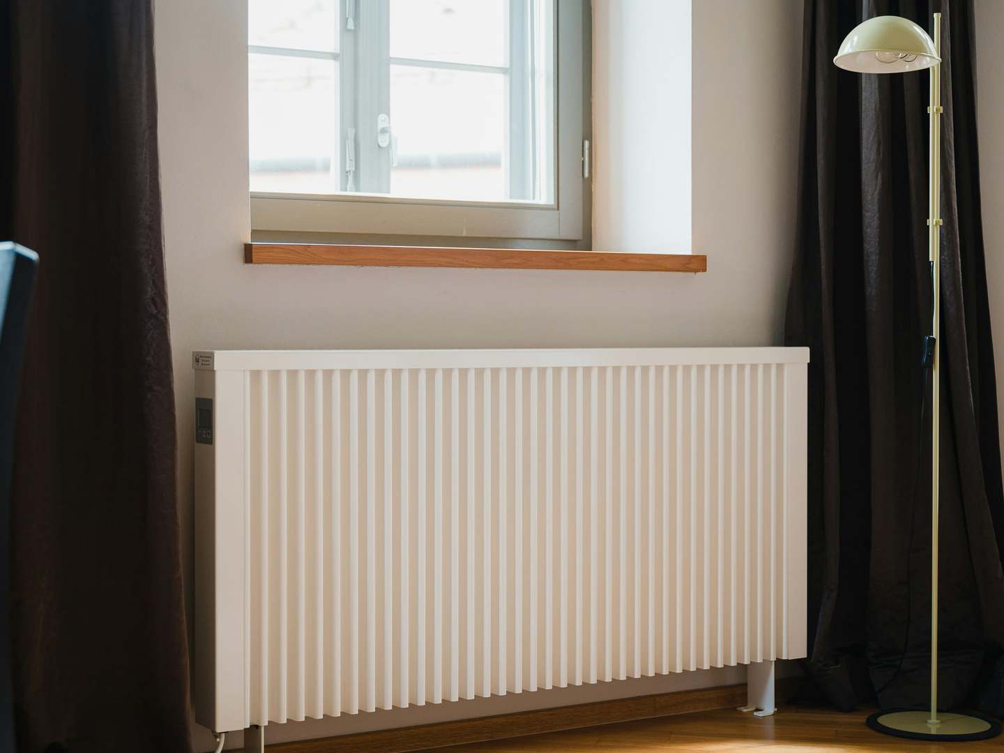 White vertical-fin radiator under a living room window, between dark curtains