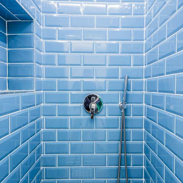 Shower wall in glossy blue metro tiles with a recessed shelf, chrome valve and hand shower