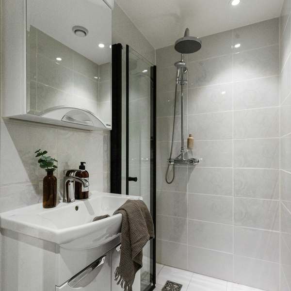 Compact shower room with large pale tiles, a black-framed glass screen and a thermostatic rainfall shower